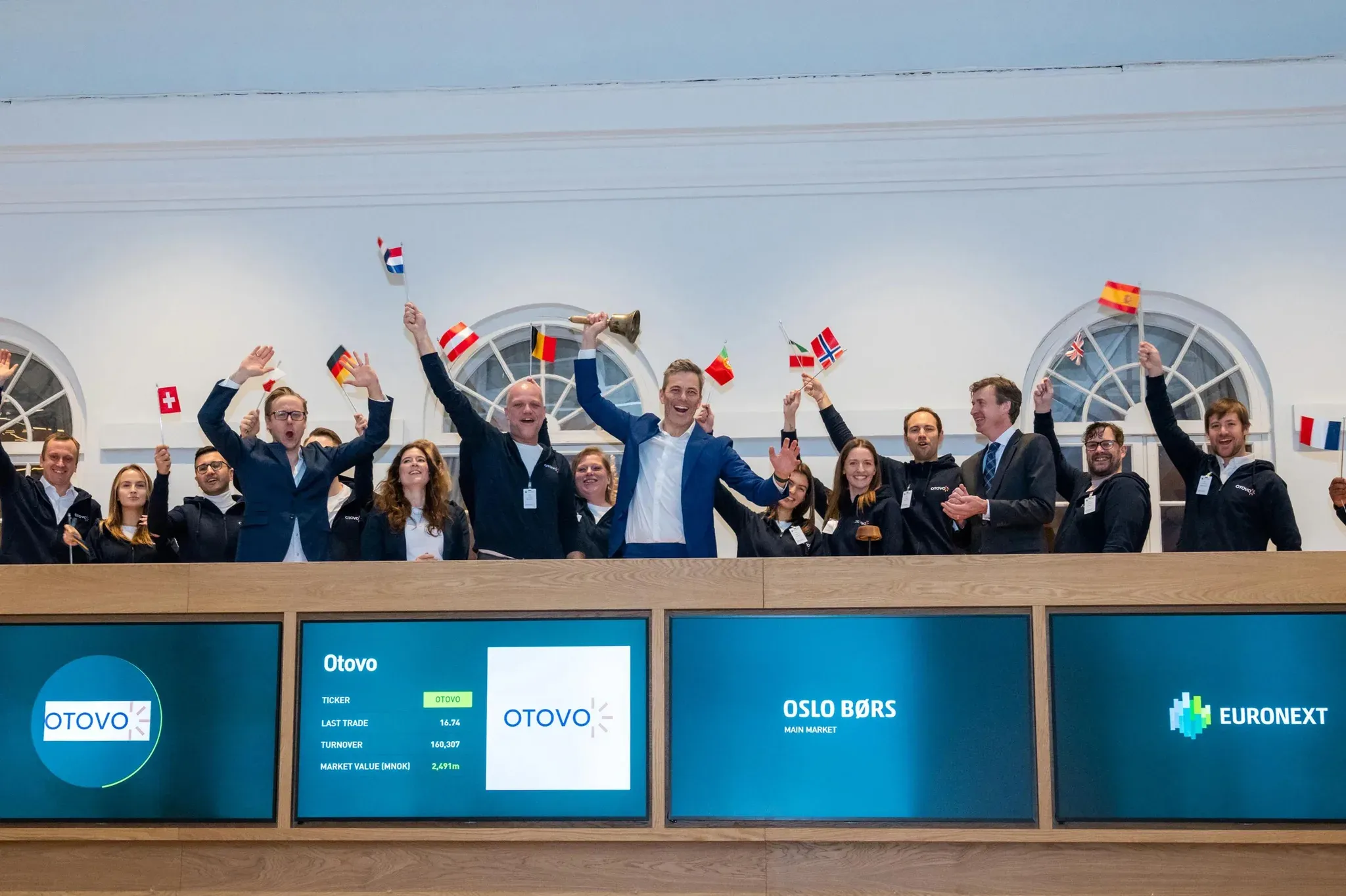 Medewerkers en het management van Otovo luiden de bel op de beurs van Oslo, terwijl ze met Europese vlaggen zwaaien.